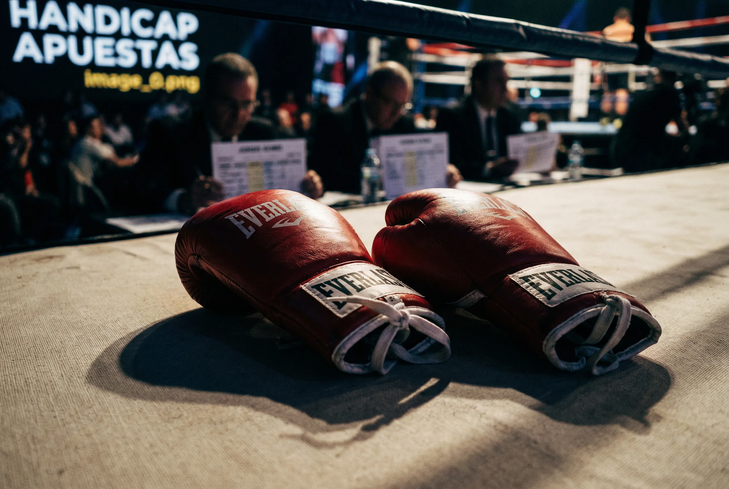 Guantes de boxeo rojos sobre un ring con tarjetas de puntuacion de jueces al fondo