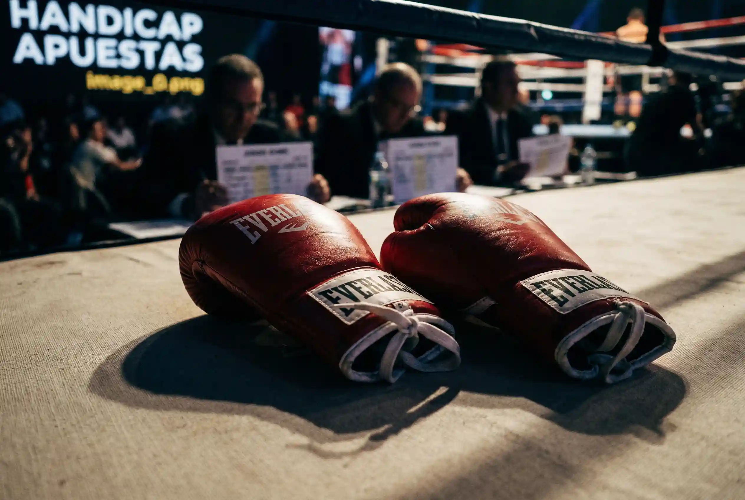 Guantes de boxeo rojos sobre un ring con tarjetas de puntuacion de jueces al fondo